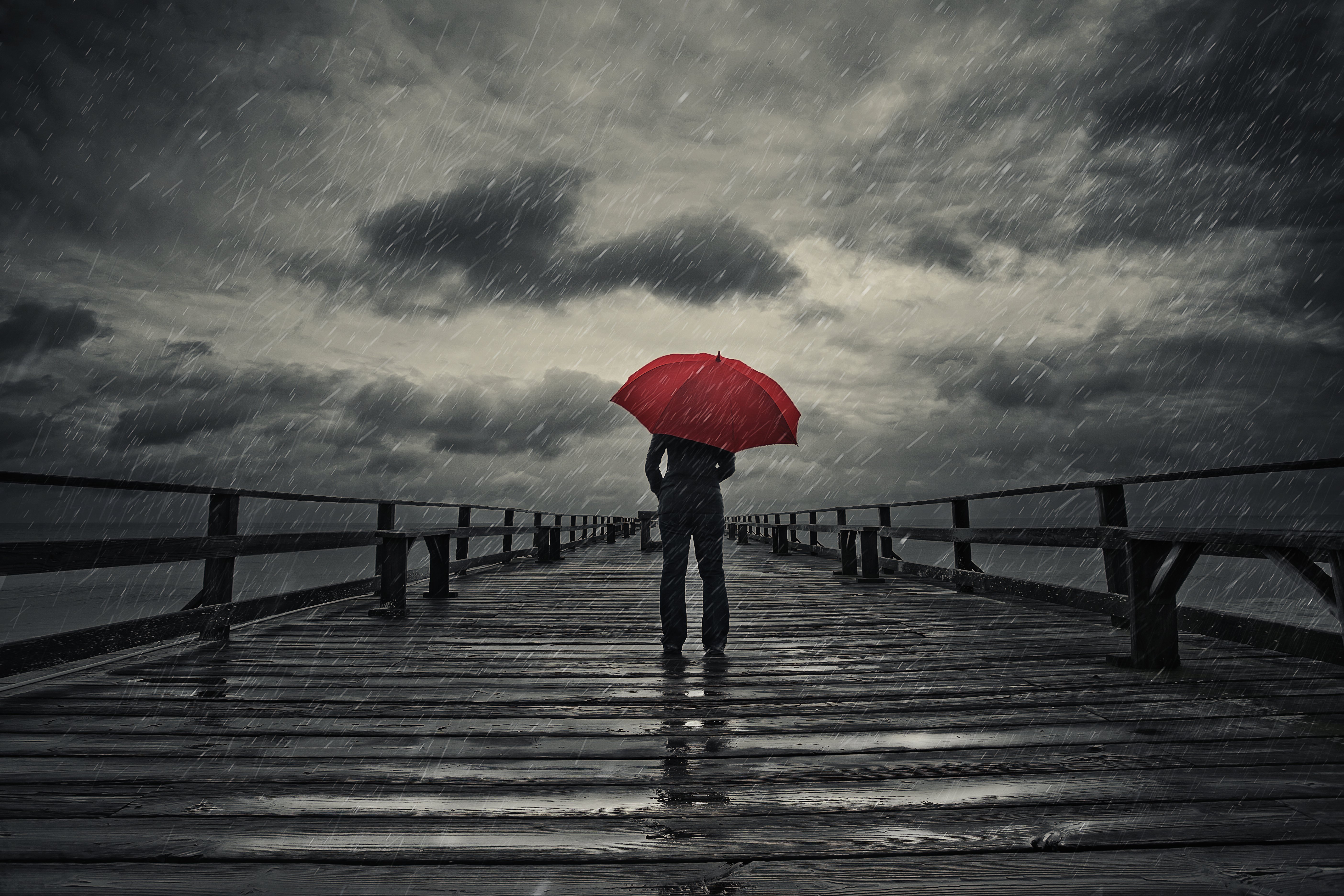 A person standing on a pier during a storm with a red umbrella